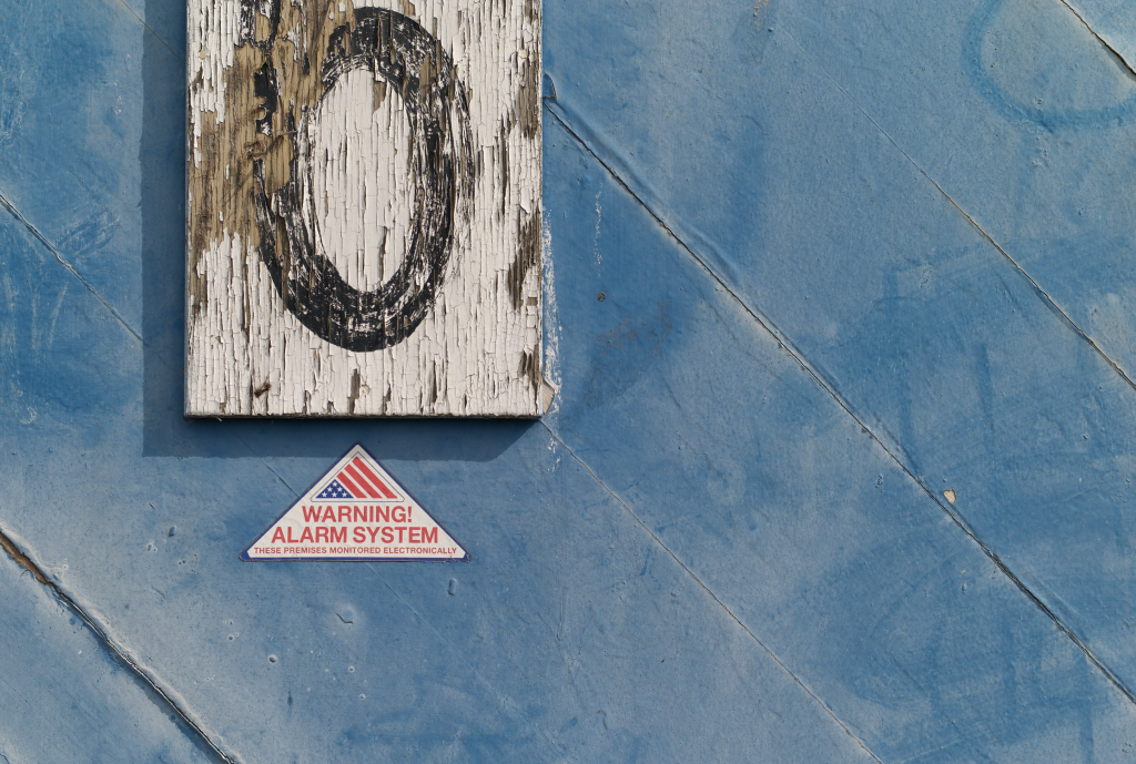 Photo of a weathered hand-painted "6" sign and a sticker reading "Warning! Alarm System" on blue painted wood