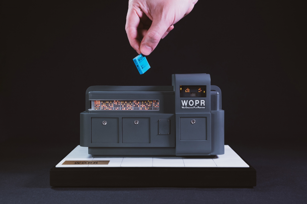 Miniature replica of WOPR, the war mainframe computer from WarGames, with artist's hand holding a tiny operations manual